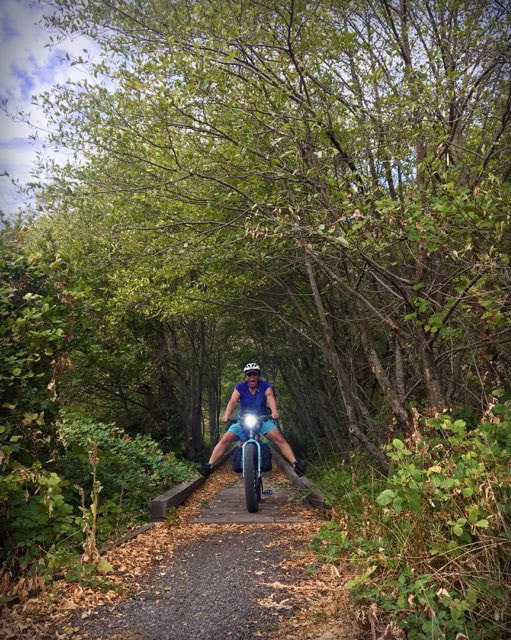 Cyclist rides over trail bridge in the woods with legs outstretched to the sides of a Surly Ice Cream Truck fat bike
