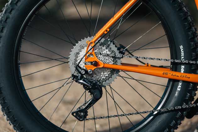 Zoomed in right side view of the rear wheel, cassette, derailleur and pulleys of a Surly Pugsley fat bike